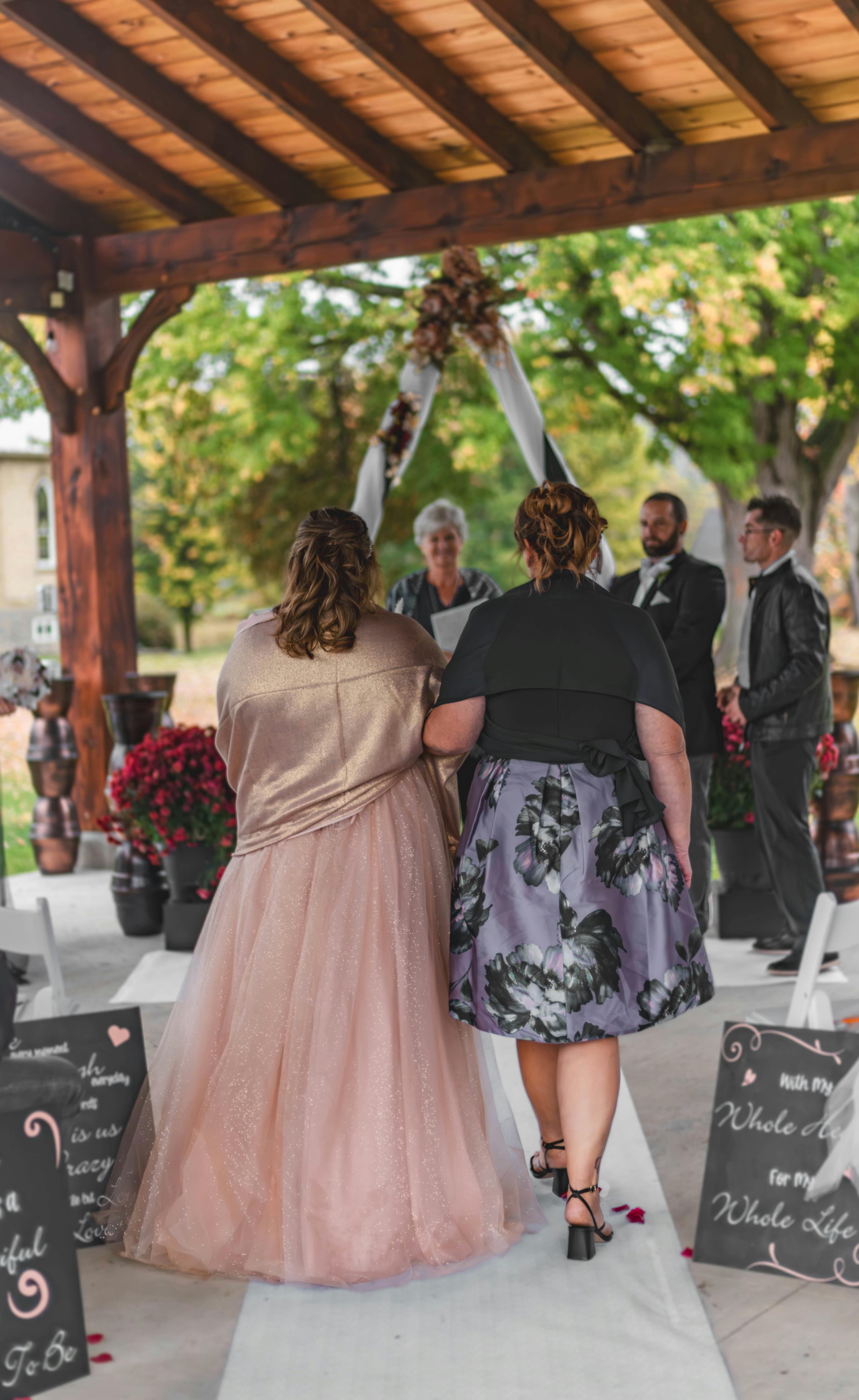 A charming outdoor wedding ceremony set under a wooden pavilion with guests and decorations.