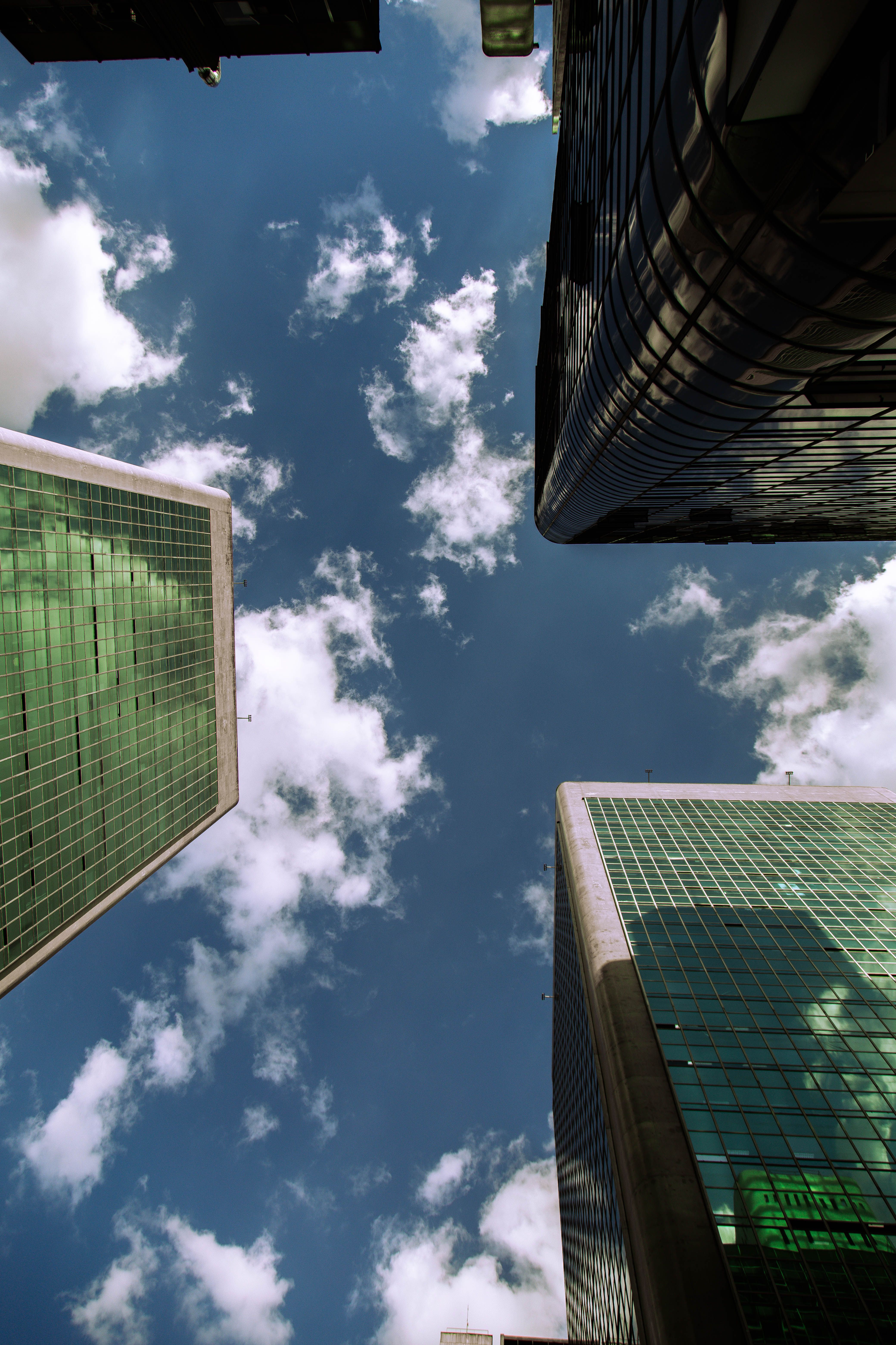 A low angle view of modern skyscrapers against a bright blue sky with clouds.